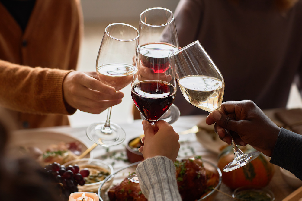 Closeup of group of people toasting with wine glasses at festive dinner table celebrating Thanksgiving together, copy space
